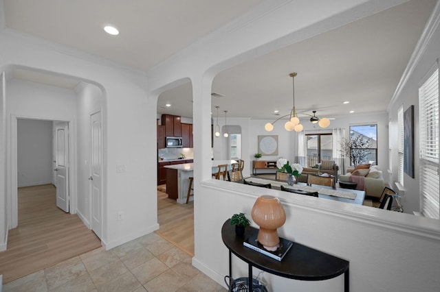kitchen with light tile patterned flooring, recessed lighting, arched walkways, ornamental molding, and stainless steel microwave