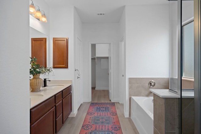 full bathroom featuring a closet, double vanity, wood finished floors, a bath, and a sink