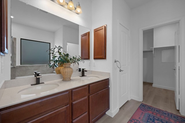 full bathroom with double vanity, visible vents, wood finished floors, and a sink