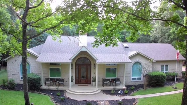 14904 Oak Shores Dr, Willis, TX 77318 - view of front facade with a front lawn, a porch, a shingled roof, and a chimney
