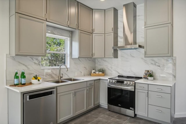 kitchen featuring gray cabinetry, a sink, appliances with stainless steel finishes, wall chimney range hood, and backsplash