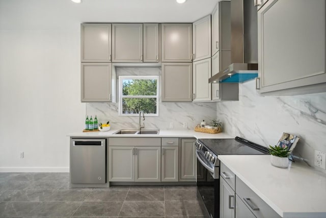 kitchen with gray cabinets, stainless steel appliances, wall chimney range hood, and a sink