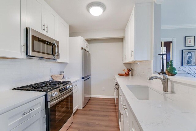 4010 Lewis Ln, Austin, TX 78756 - kitchen featuring appliances with stainless steel finishes, backsplash, white cabinets, light wood-type flooring, and light stone countertops