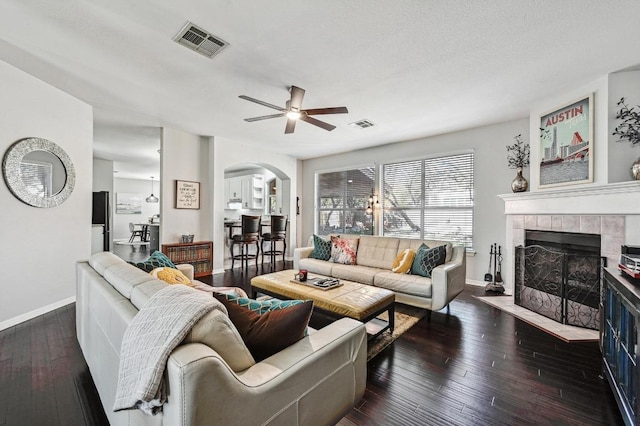 living room featuring a ceiling fan, hardwood / wood-style floors, arched walkways, a tile fireplace, and visible vents
