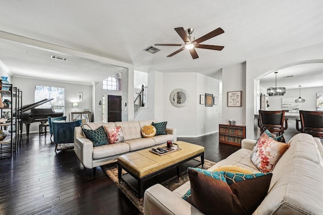 living area with stairs, ceiling fan, arched walkways, dark wood-style flooring, and visible vents