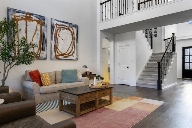 living room with wood finished floors, baseboards, a high ceiling, stairway, and arched walkways