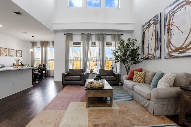 living area featuring a high ceiling, a chandelier, wood finished floors, and visible vents