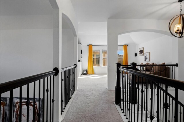 corridor with carpet floors, a notable chandelier, arched walkways, and an upstairs landing