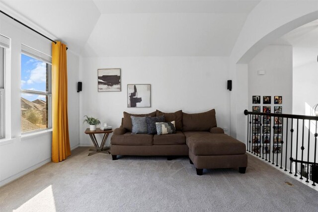 carpeted living room featuring arched walkways and vaulted ceiling