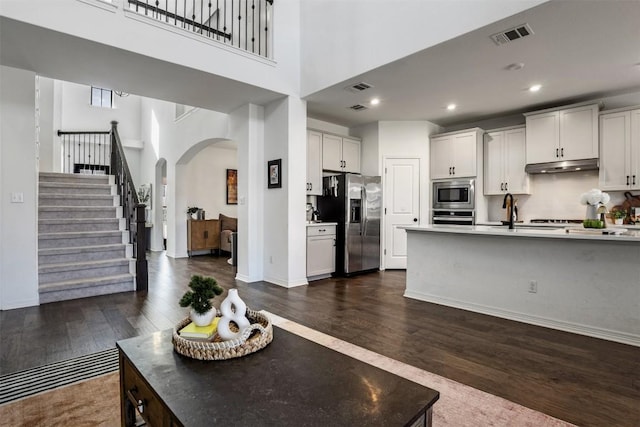 kitchen featuring visible vents, under cabinet range hood, arched walkways, dark wood finished floors, and appliances with stainless steel finishes