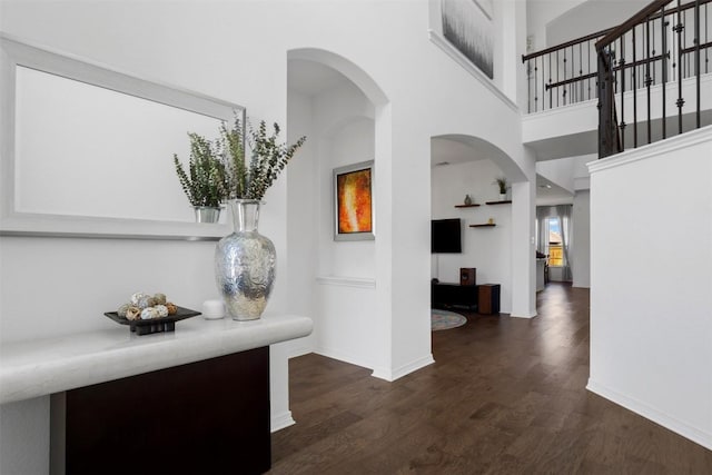 corridor with baseboards, arched walkways, dark wood finished floors, and a towering ceiling