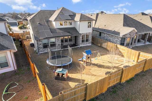 rear view of house featuring a residential view, roof with shingles, a trampoline, stone siding, and solar panels