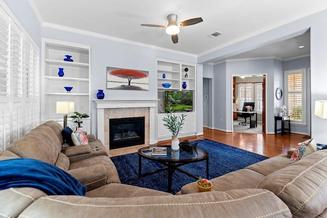 100 Blacksmiths Cir, Georgetown, TX 78633 - living area featuring wood finished floors, built in features, ceiling fan, a tiled fireplace, and crown molding