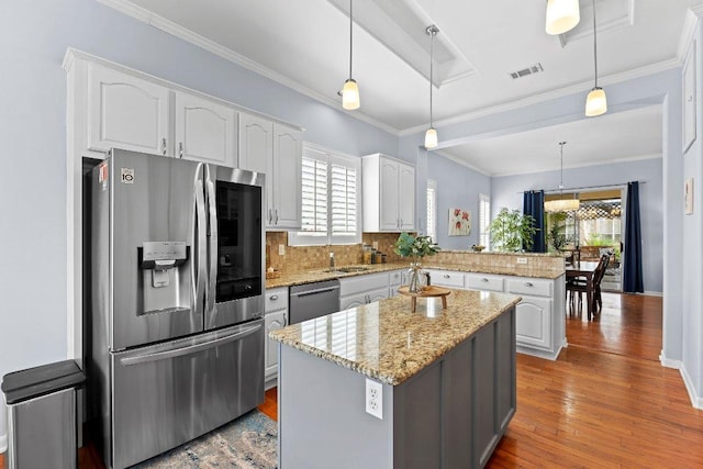 100 Blacksmiths Cir, Georgetown, TX 78633 - kitchen featuring stainless steel appliances, a peninsula, white cabinets, wood finished floors, and ornamental molding