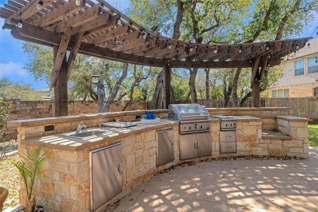 view of patio / terrace featuring exterior kitchen, a sink, a grill, a fenced backyard, and a pergola