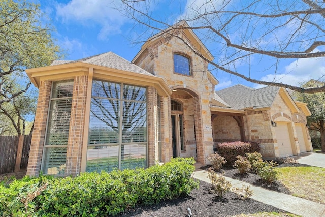 view of front facade featuring fence, brick siding, stone siding, an attached garage, and roof with shingles