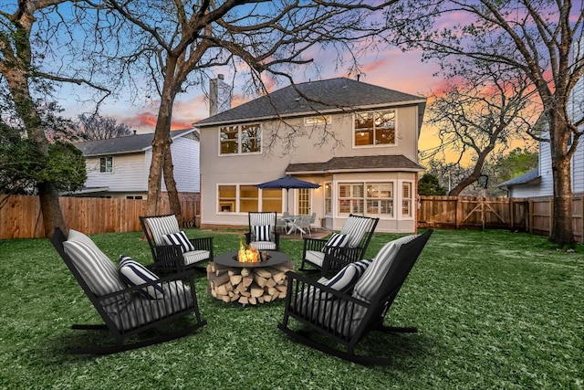 back of property at dusk with a lawn, a fenced backyard, a fire pit, and stucco siding