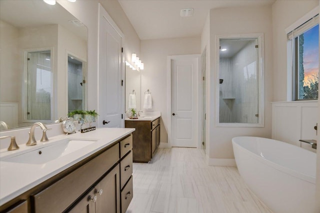 full bathroom featuring a soaking tub, a stall shower, two vanities, and a sink