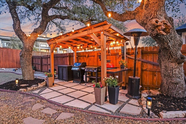 patio terrace at dusk featuring grilling area and a fenced backyard