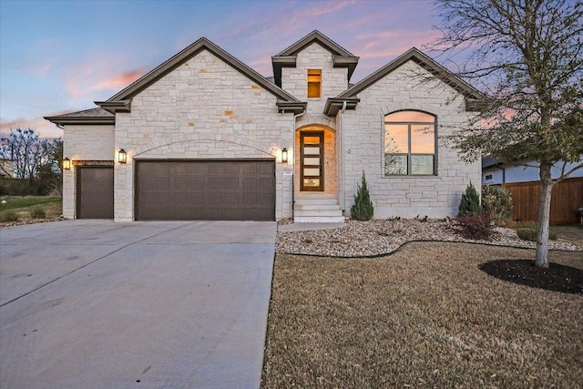 french country style house with stone siding, fence, concrete driveway, and a garage