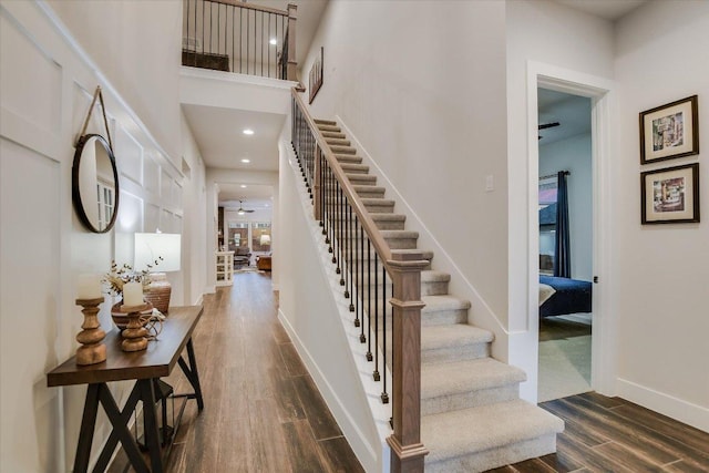 stairs with baseboards, recessed lighting, wood finished floors, and a high ceiling