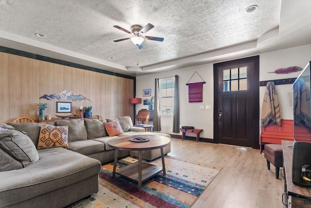 130 Holbox Dr, Del Valle, TX 78617 - living area featuring a textured ceiling, a raised ceiling, a ceiling fan, light wood-style flooring, and wooden walls