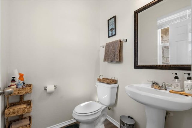 half bath with toilet, baseboards, and a sink