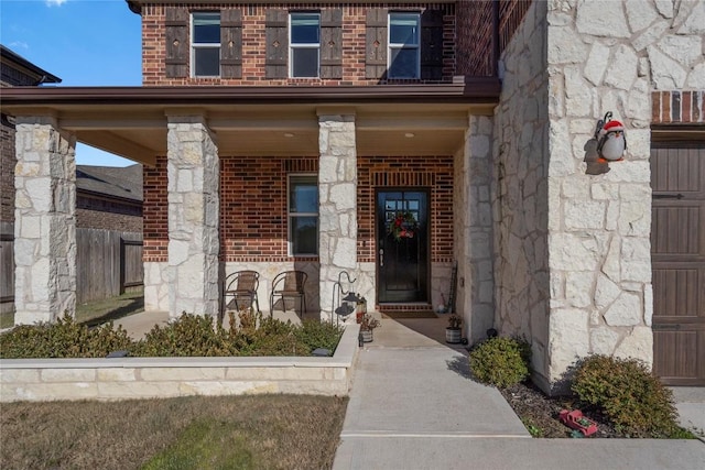 view of exterior entry featuring brick siding, covered porch, and stone siding