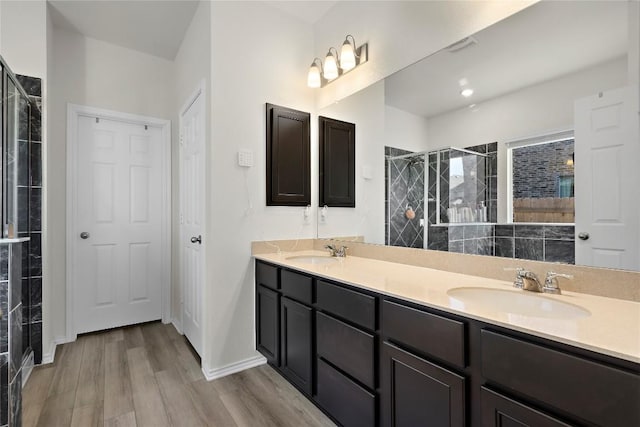 bathroom with double vanity, a stall shower, wood finished floors, and a sink