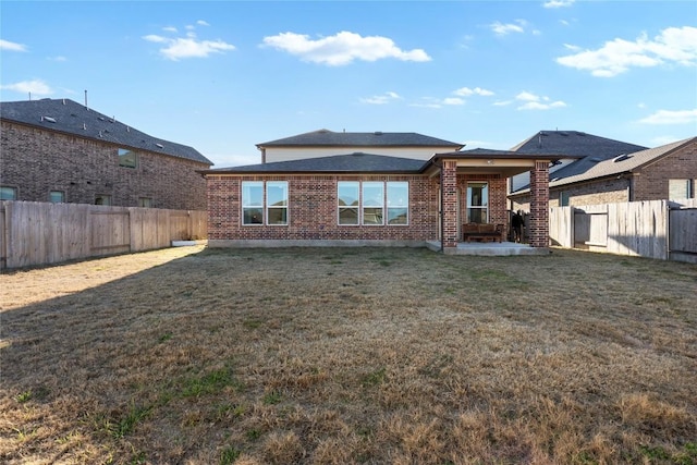 back of property featuring a yard, brick siding, and a fenced backyard