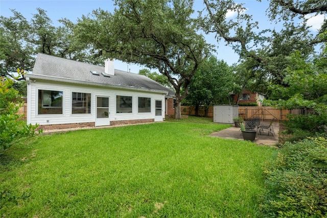 rear view of property with a lawn, a chimney, a fenced backyard, an outdoor structure, and a patio