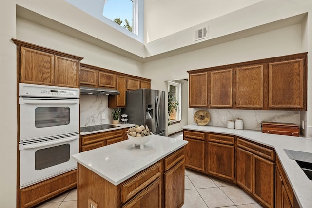 kitchen with white double oven, a high ceiling, under cabinet range hood, stainless steel fridge, and black electric stovetop