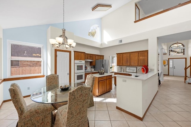 kitchen with stainless steel fridge, a chandelier, light countertops, brown cabinetry, and white double oven