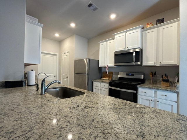 kitchen with visible vents, a sink, stainless steel appliances, white cabinets, and light stone countertops