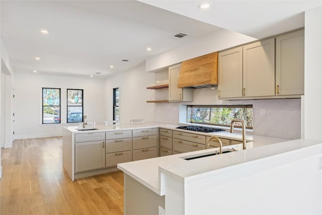 kitchen with light wood finished floors, a peninsula, black gas stovetop, custom range hood, and recessed lighting