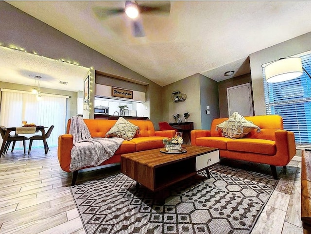 living room with visible vents, a ceiling fan, a textured ceiling, light wood finished floors, and vaulted ceiling