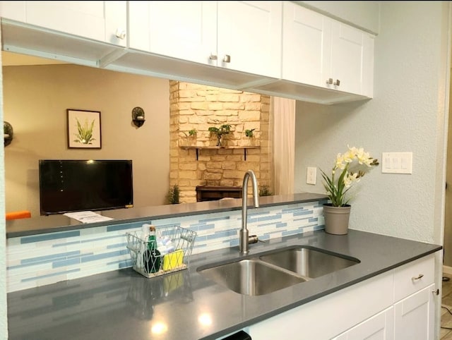 kitchen featuring a sink, tasteful backsplash, dark countertops, and white cabinets