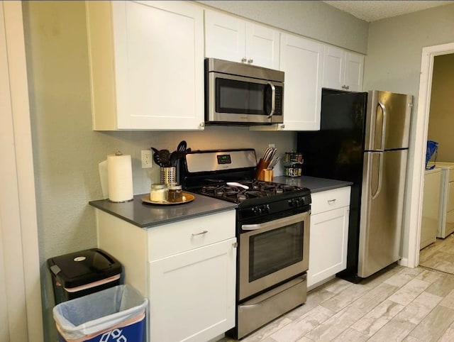 kitchen with stainless steel appliances, dark countertops, washing machine and dryer, and white cabinets