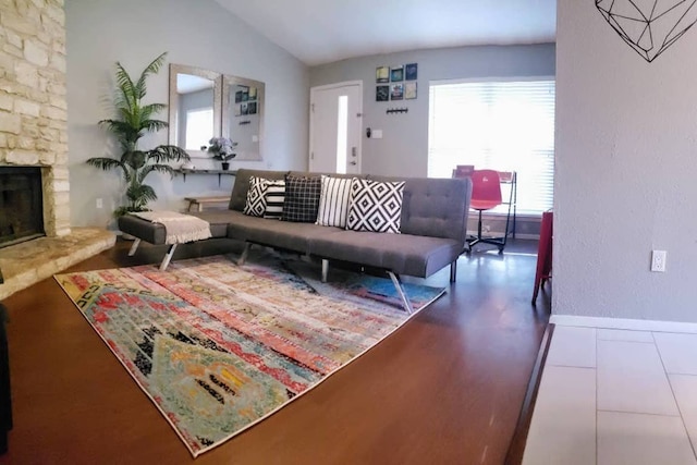 living area with a stone fireplace, lofted ceiling, wood finished floors, and baseboards