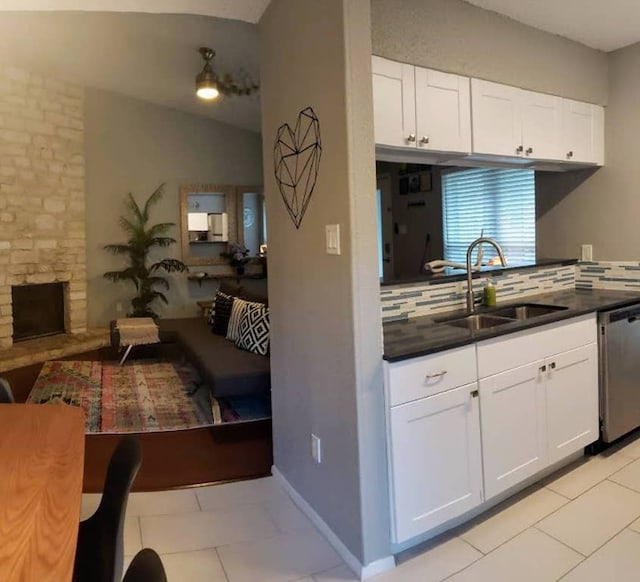 kitchen featuring a sink, stainless steel dishwasher, dark countertops, open floor plan, and white cabinetry
