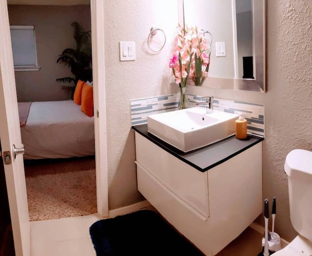 ensuite bathroom with vanity, toilet, a textured wall, and connected bathroom