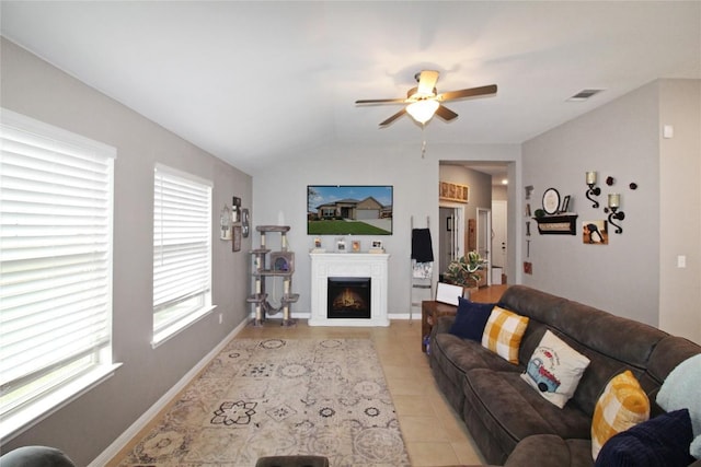 180 Sunshine Ln, Kyle, TX 78640 - living room with ceiling fan, visible vents, vaulted ceiling, light tile patterned floors, and a warm lit fireplace