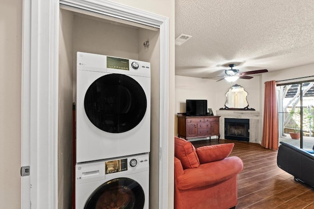 9226 Jollyville Rd Unit 170, Austin, TX 78759 - laundry room featuring stacked washer and clothes dryer, a textured ceiling, a ceiling fan, a fireplace, and dark wood-type flooring