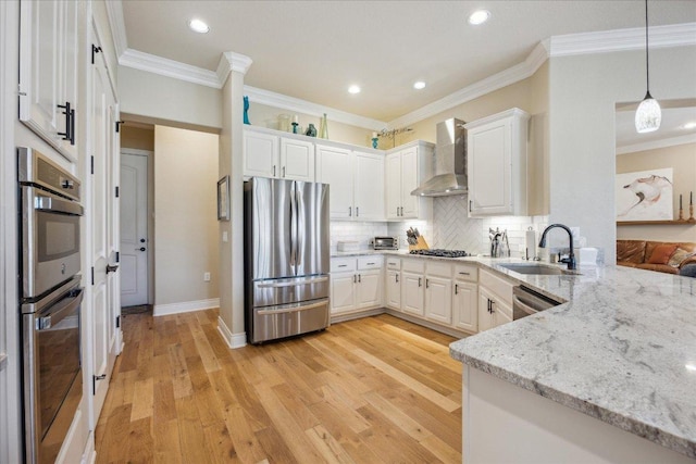 kitchen with a sink, wall chimney range hood, ornamental molding, white cabinetry, and stainless steel appliances