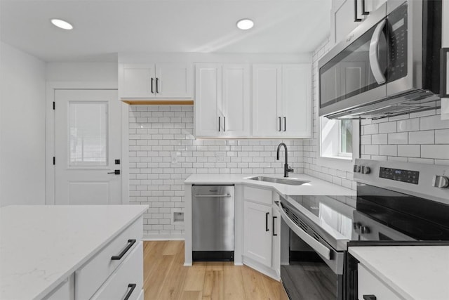 kitchen with a sink, backsplash, stainless steel appliances, white cabinets, and light wood finished floors