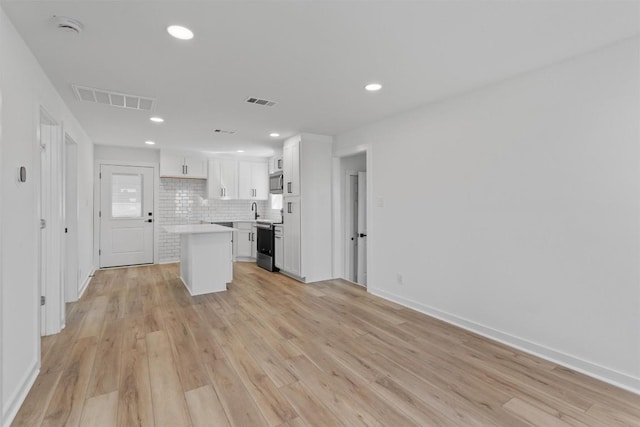 kitchen featuring visible vents, light wood-style flooring, a kitchen island, white cabinetry, and decorative backsplash