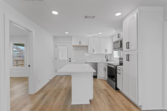 kitchen featuring visible vents, light wood-style flooring, backsplash, appliances with stainless steel finishes, and white cabinets
