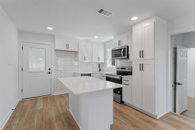 kitchen featuring visible vents, light wood-style flooring, appliances with stainless steel finishes, white cabinetry, and a center island