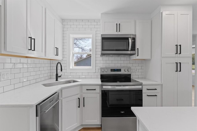 kitchen with light countertops, decorative backsplash, appliances with stainless steel finishes, white cabinets, and a sink