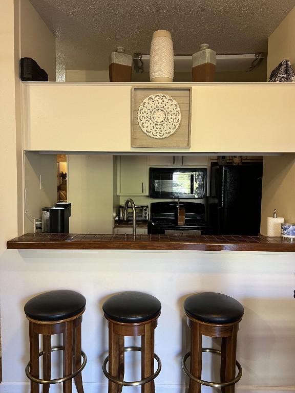 2905 Swisher St Unit 207, Austin, TX 78705 - kitchen featuring black appliances, a kitchen bar, and tile counters